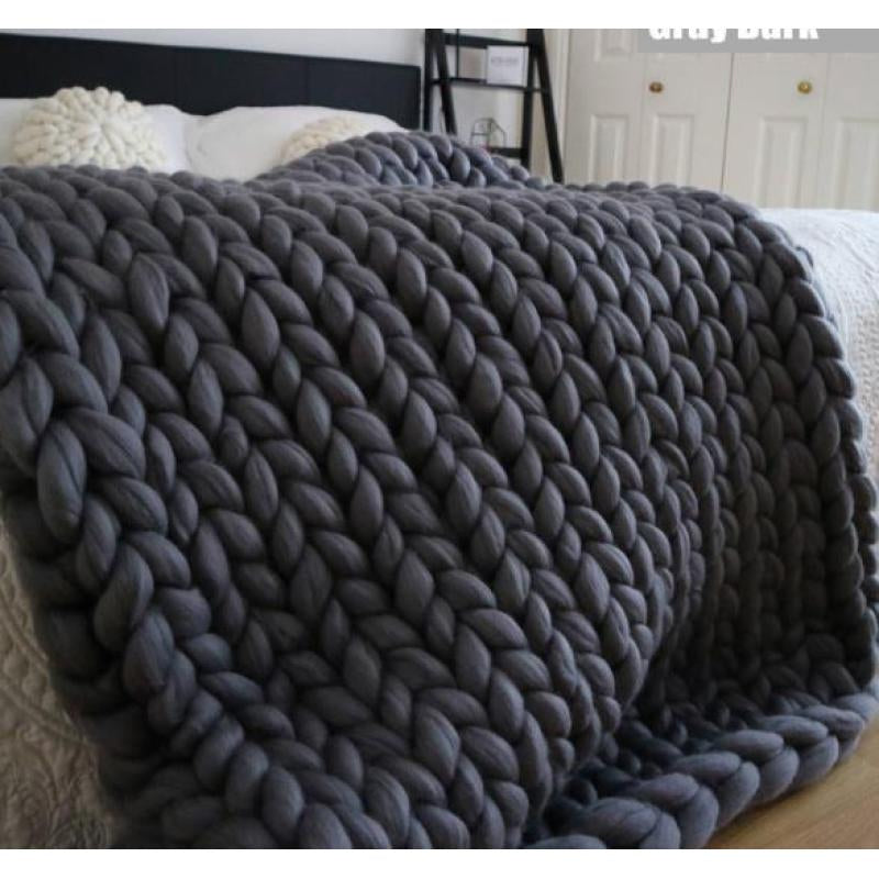 Gray knitted blanket draped over a bed in a bedroom setting.